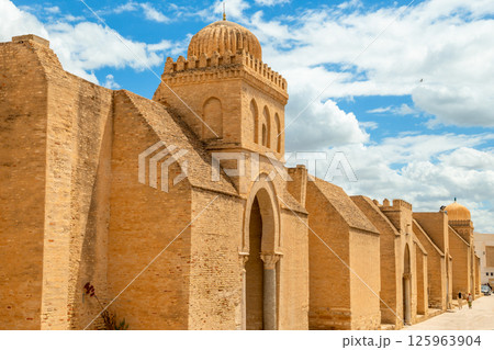 Ancient walls and dome of the Great Mosque of Uqba with clouds in the blue sky, Kairouan, Tunisia Ancient walls and dome of the Great Mosque of Uqba with clouds in the blue sky, Kairouan, Tunisia 125963904