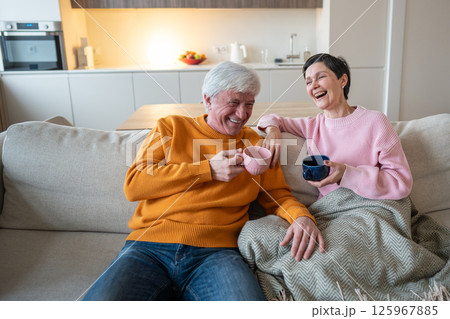 Happy laughing husband and wife couple enjoying tea time together on cozy couch in living room 125967885