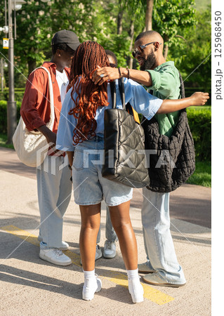 Excited happy group of African university students cheerfully greeting one another with hugs in park 125968450