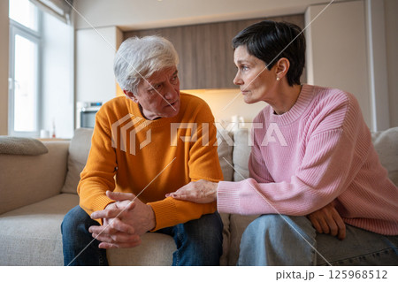 Loving wife holding hands with distressed serious husband on couch offering emotional support Loving wife holding hands with distressed serious husband on couch offering emotional support 125968512