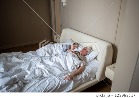 Peaceful mature husband and wife sleeping soundly while embraced together in cozy bedroom together Peaceful mature husband and wife sleeping soundly while embraced together in cozy bedroom together 125968517