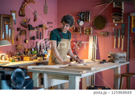 Skilled woodworker carpenter plans furniture assembly searching for tools in busy joinery workshop  125968689