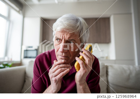 Serious elderly man appears suspicious and fearful, speaking on phone at home. Scam, fraud phobia Serious elderly man appears suspicious and fearful, speaking on phone at home. Scam, fraud phobia 125968964