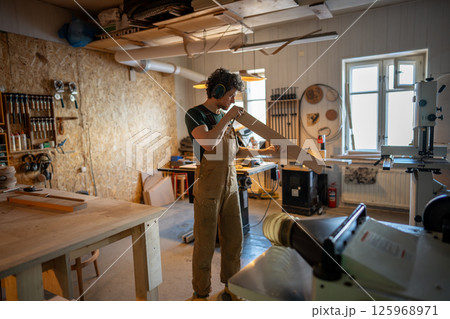 Professional meticulous carpenter inspecting wooden beam quality before workshop processing 125968971