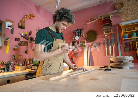 Resting relaxed woodworker taking break in workshop, check smartphone waiting for customers Resting relaxed woodworker taking break in workshop, check smartphone waiting for customers 125969082