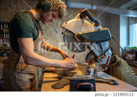 Skilled carpenter use miter saw, measure and trim wood beams in workshop. Handyman precision cut Skilled carpenter use miter saw, measure and trim wood beams in workshop. Handyman precision cut 125969113