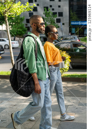 Serious boyfriend, cheerful girlfriend on date. Black couple holding hands wander, walk around town. 125969114