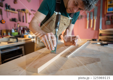 Skilled serious craftsman carpenter meticulously refining board texture using precise chisel work Skilled serious craftsman carpenter meticulously refining board texture using precise chisel work 125969115