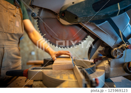 Craftsman operates mitre saw with circular blade to slice wooden beam. Handmade furniture projects 125969123