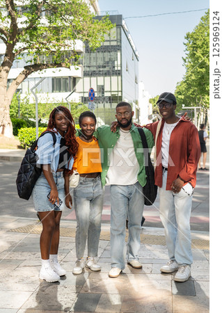 Happy young multicultural group of friends stand together, hugging and smiling at camera on walk Happy young multicultural group of friends stand together, hugging and smiling at camera on walk 125969124