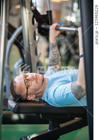 Focused exhausted determined man lift barbell for strength training in gym. Sportsman look at camera Focused exhausted determined man lift barbell for strength training in gym. Sportsman look at camera 125969226