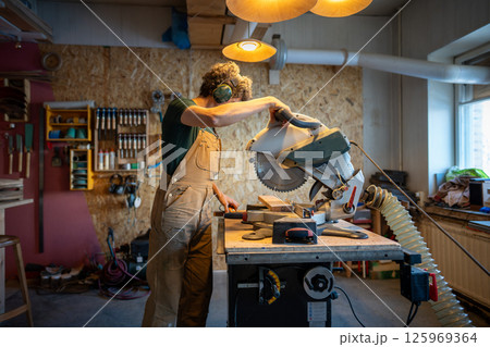 Meticulous craftsman carefully maneuvers mitre saw cutting wood beams. Joinery smoothing techniques 125969364