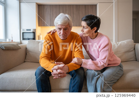 Sad frustrated mature couple sharing emotional struggle as wife consoles husband, life difficulties 125969440