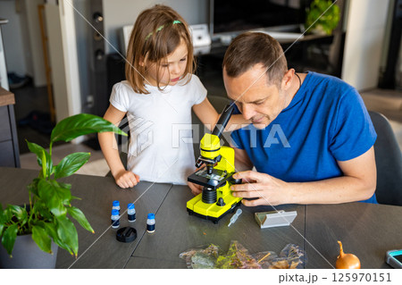 Father and daughter examining various plant samples under a microscope at home. Concept of family science education and botanical exploration 125970151