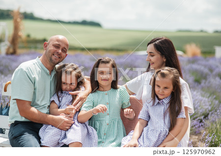 A family sits on a bench in the middle of a lavender field.  125970962