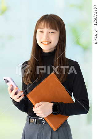 スマートフォンとバインダーを持つ笑顔の女性・ビジネスウーマン スマートフォンとバインダーを持つ笑顔の女性・ビジネスウーマン 125971557