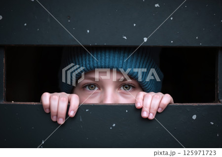 A child peeking through a fence. 125971723