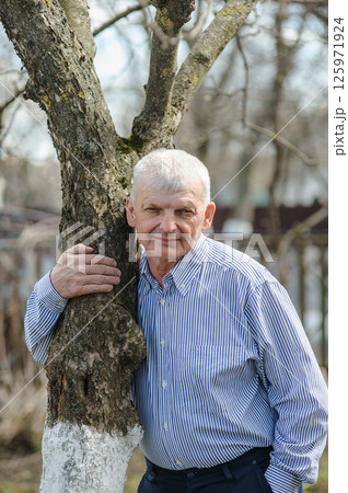 An old man is having a rest in the park. A pensioner near a tree smiles beautifully. An old man is having a rest in the park. A pensioner near a tree smiles beautifully. 125971924