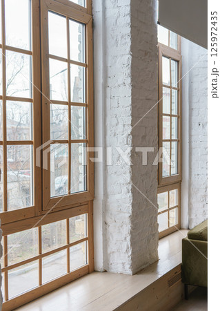 Large windows with wooden frames in loft interior with white brick walls inside apartment or house 125972435