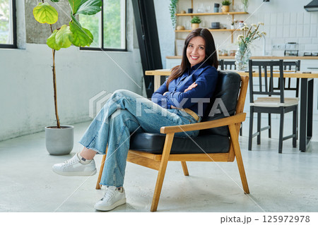 Portrait of beautiful 30s smiling woman sitting in armchair at home in living room 125972978