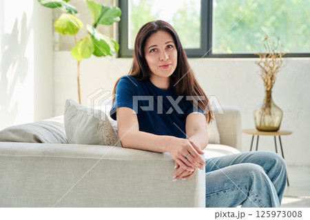 Portrait of beautiful young brunette woman sitting on sofa in living room 125973008