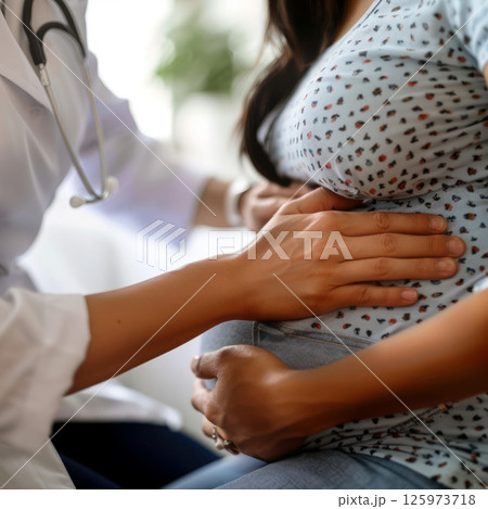 A doctor gently palpates a pregnant woman's abdomen during a prenatal checkup, demonstrating compassionate care 125973718