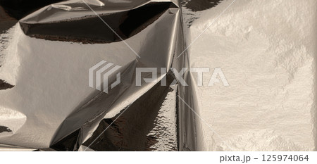 Silver foil with shiny, metallic texture creates a smooth, reflective surface. Crinkled and folded 125974064