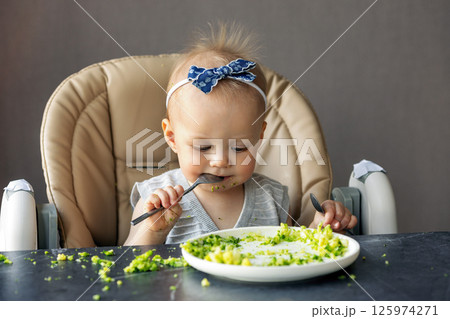 Adorable Baby Girl Enjoying Healthy Meal, Eating broccoli with spoon and Making Mess, Happy Infant, Toddler First Foods. Child eating vegetables Adorable Baby Girl Enjoying Healthy Meal, Eating broccoli with spoon and Making Mess, Happy Infant, Toddler First Foods. Child eating vegetables 125974271