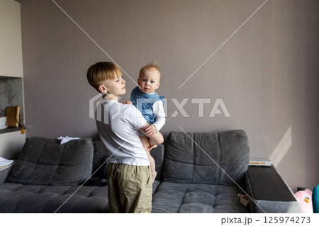 Adorable young boy holding baby sister at home, authentic candid moment of sibling bonding, love and care. Family connection in natural light, everyday childhood scene, real-life. Portrait of children 125974273