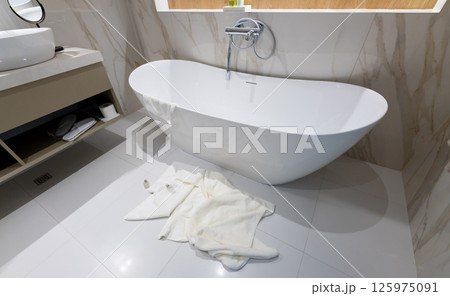 A modern freestanding bathtub in a luxury bathroom with towels left on the floor A modern freestanding bathtub in a luxury bathroom with towels left on the floor 125975091