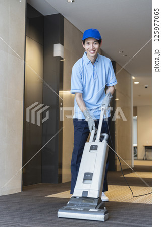 業務用カーペット用掃除機で作業をする若い男性クリーニングスタッフ　カメラ目線 125977065