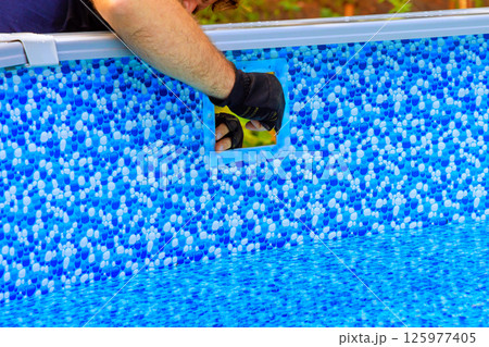Worker carefully installs component into filtration system newly set up above ground pool on swimming pool backyard setting 125977405