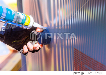 Worker seals connection on pool liner with caulking gun at construction site. Worker seals connection on pool liner with caulking gun at construction site. 125977406