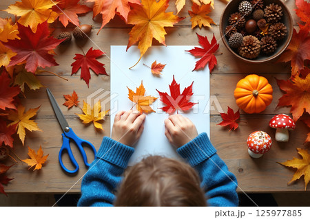 Child crafting with autumn leaves on a wooden table. 125977885