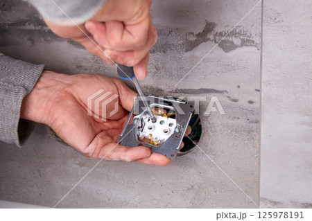 A worker installs an electrical outlet into a wall using a screwdriver 125978191