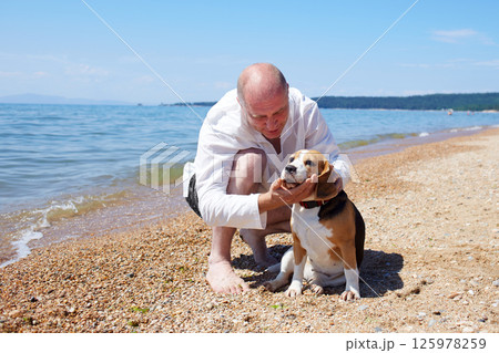 A happy man enjoys a sunny day on the sea beach with his beagle dog on a warm summer day 125978259