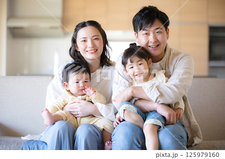 木のぬくもりのある新築のような家の自宅のソファーでくつろぐ4人の日本人家族　カメラ目線の笑顔 125979160