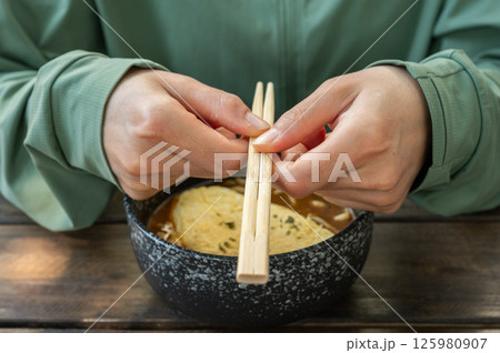 Cropped shot view of woman holding chopsticks before eating Udon. Udon is a thick, white, ribbon-like noodle popular in Japanese cuisine. 125980907