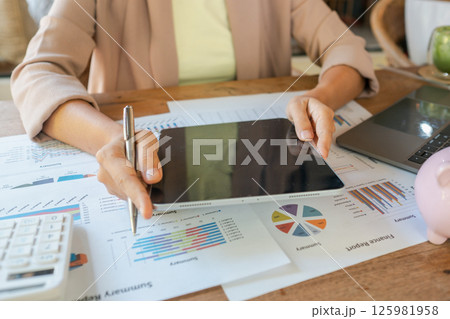 Professional woman using tablet to review financial charts and graphs at work desk, focusing on business strategy and analysis. 125981958
