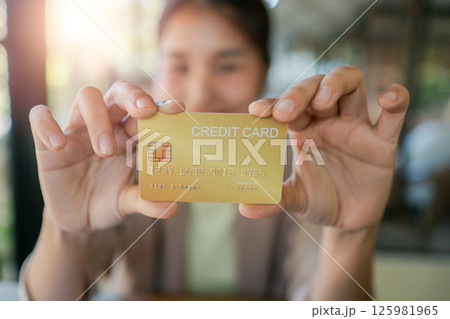 Close-up of a woman holding a gold credit card, showcasing financial concepts in a bright, sunlit cafe environment. 125981965