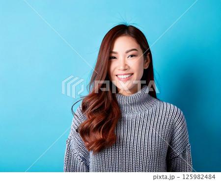 微笑みを浮かべている長い髪の若い女性、青背景 125982484