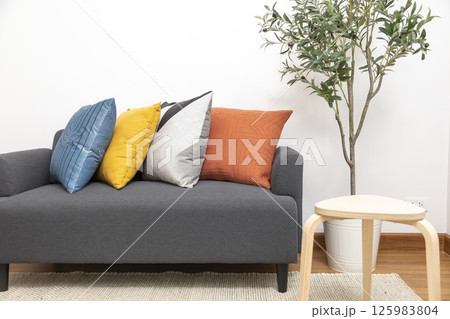 Stylish living room interior with orange, red blue, yellow pillow on sofa, wooden coffee table and olive tree in a pot. Stylish living room interior with orange, red blue, yellow pillow on sofa, wooden coffee table and olive tree in a pot. 125983804