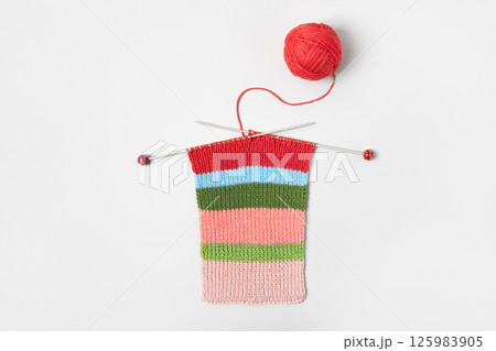 Striped piece of knitted fabric for future clothing with knitting needles and yellow ball of thread on gray background. Homemade needlework and knitting of warm, clothes and toys. Concept creativity 125983905