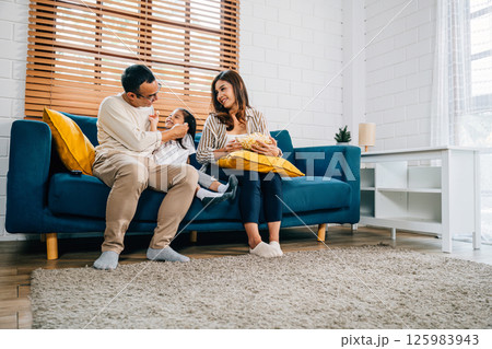 In their warm home family finds joy in watching TV and sharing popcorn. father mother daughter and sibling are all smiles creating an atmosphere of togetherness and happiness. In their warm home family finds joy in watching TV and sharing popcorn. father mother daughter and sibling are all smiles creating an atmosphere of togetherness and happiness. 125983943