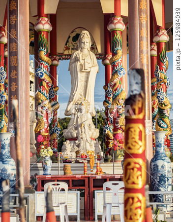 Large statue of Guanyin in colorful temple with dragon columns during sunny afternoon. Sriracha, Thailand. Large statue of Guanyin in colorful temple with dragon columns during sunny afternoon. Sriracha, Thailand. 125984039