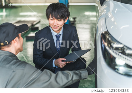 車の傷・凹みを確認する整備士の男性とスーツ姿のセールスマン 125984388