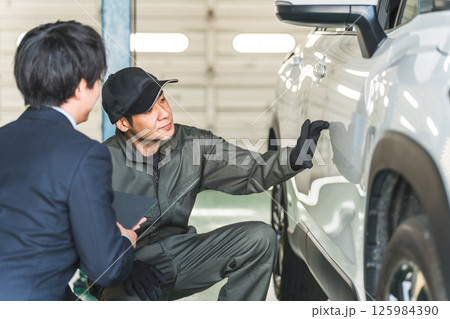 車の傷・凹みを確認する整備士の男性とスーツ姿のセールスマン 車の傷・凹みを確認する整備士の男性とスーツ姿のセールスマン 125984390
