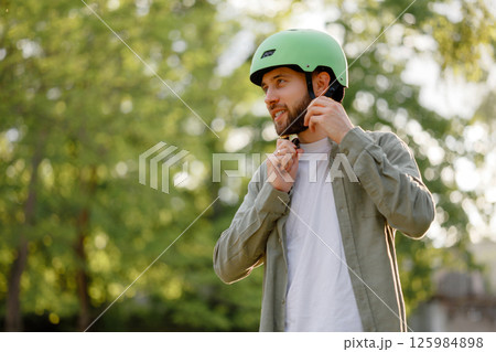 Man putting on a green helmet while preparing for a biking adventure in a sunny park during the afternoon Man putting on a green helmet while preparing for a biking adventure in a sunny park during the afternoon 125984898