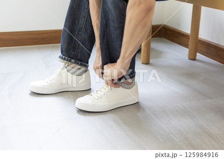 Man tie the shoelace of white sneakers sit on wood bench at home. 125984916