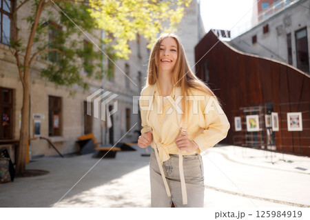 Young woman smiling in light clothing enjoys a sunny day in an urban courtyard with art installations 125984919